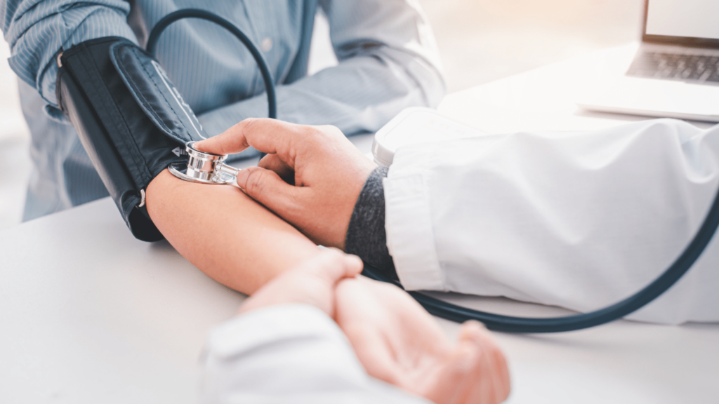 A doctor holds a stethoscope to a patient’s arm that has a blood pressure cuff on it.