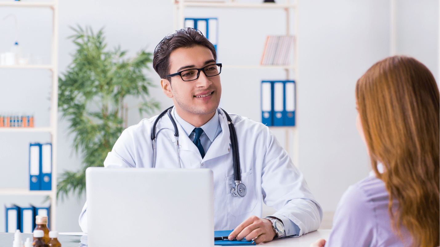 A patient sits behind a desk and listens to a patient sitting in front of them.