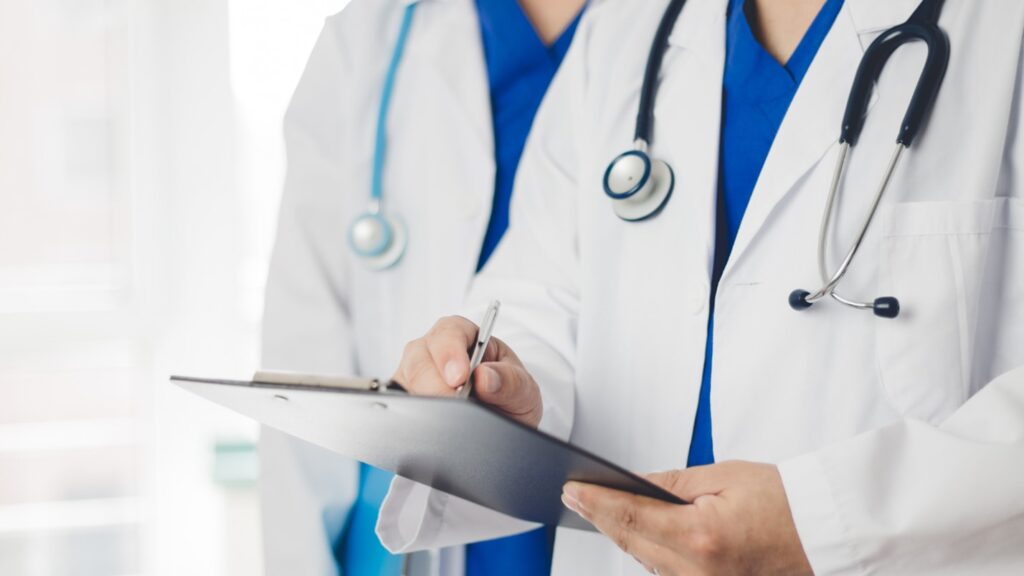 A doctor in a lab coat writes something on a clipboard.