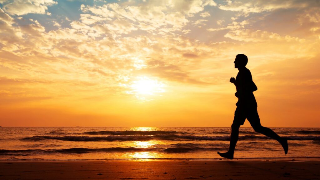 The silhouette of a man running on a beach in the sunset.