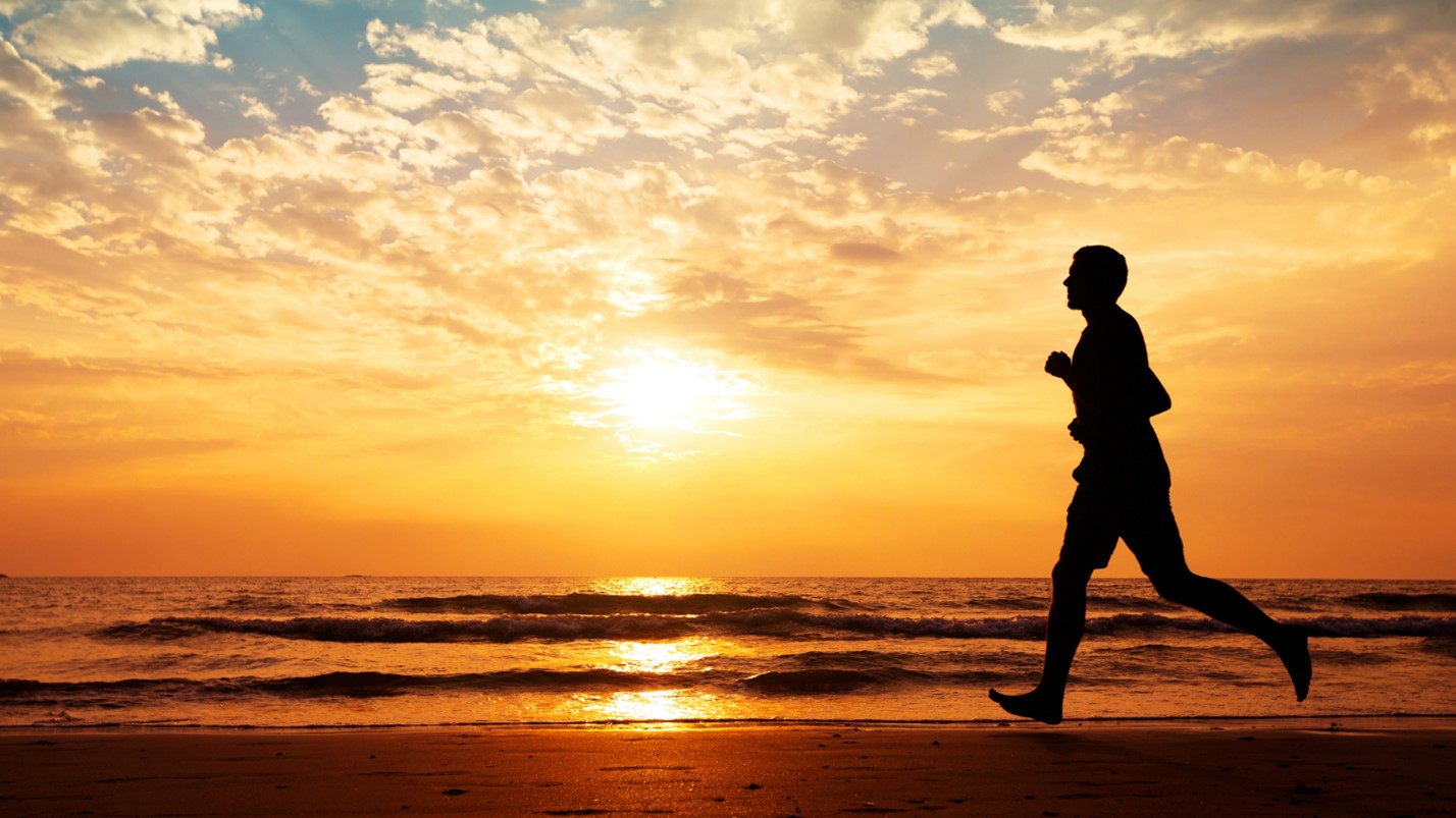 The silhouette of a man running on a beach in the sunset.